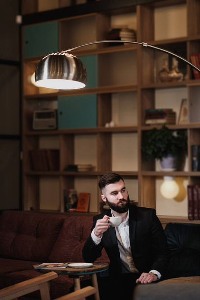 Portrait of a young handsome bearded man. A businessman in a suit sits at a table in a cafe or restaurant. - Fotó, kép