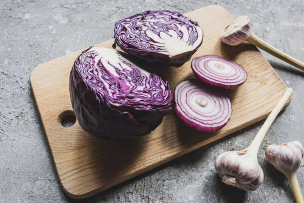 red cabbage, onion and garlic on wooden cutting board on grey concrete surface - Φωτογραφία, εικόνα