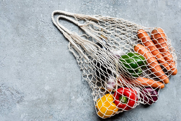top view of fresh ripe vegetables in string bag on grey concrete surface - Valokuva, kuva
