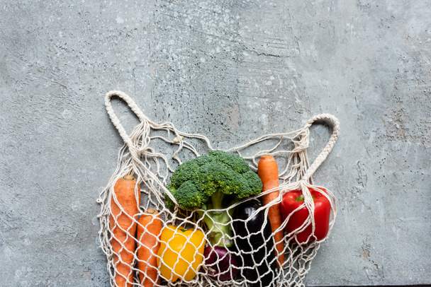 top view of fresh ripe vegetables in string bag on grey concrete surface - Fotoğraf, Görsel
