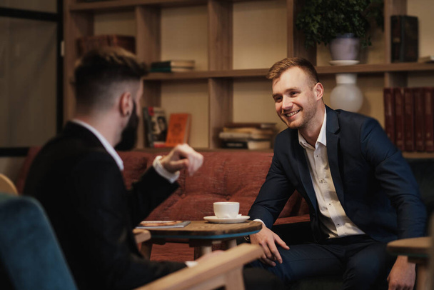 Two men in suits sit in a restaurant. A business meeting. Men drink coffee. - Φωτογραφία, εικόνα
