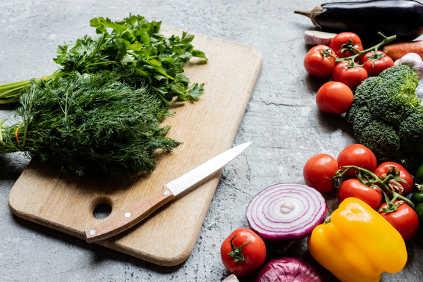 verduras maduras frescas coloridas cerca de la tabla de cortar con cuchillo en la superficie de hormigón gris
 - Foto, imagen