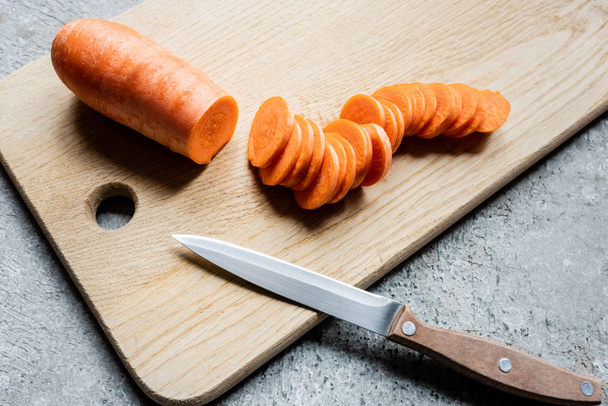 fresh ripe carrot slices on wooden cutting board with knife on concrete surface - Fotoğraf, Görsel