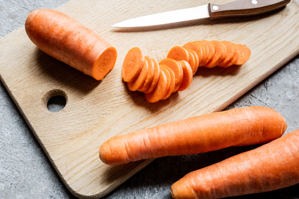 fresh ripe carrot slices on wooden cutting board with knife on concrete surface - Foto, imagen