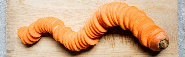 top view of fresh ripe carrot slices on wooden cutting board on concrete surface, panoramic crop - Foto, Imagen