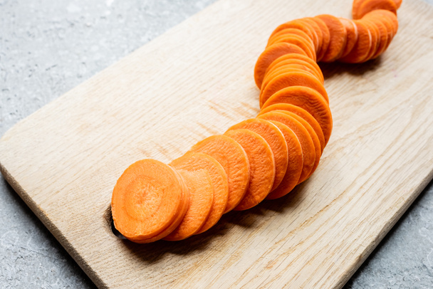 fresh ripe carrot slices on wooden cutting board on concrete surface - Фото, изображение