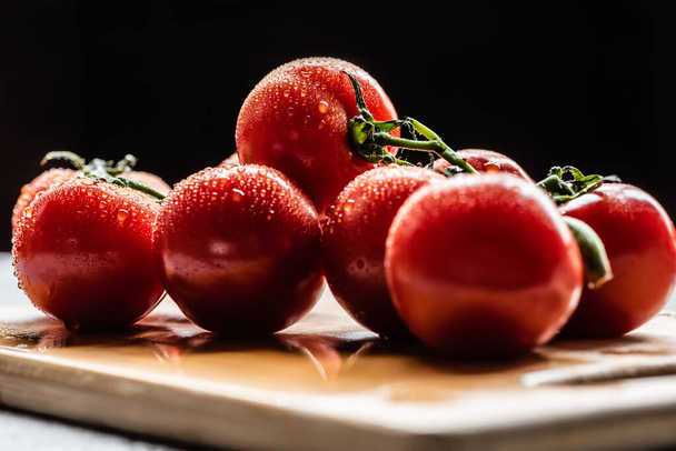 φρέσκες ώριμες κόκκινες ντομάτες σε κλαδί με σταγόνες νερού σε ξύλινη σανίδα που απομονώνονται σε μαύρο - Φωτογραφία, εικόνα