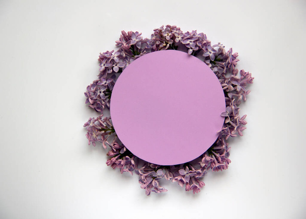 Creatieve platte lay compositie met ronde papieren kaart en bloeiende paarse lila met groene bladeren. Voorjaarsconcept. Natuur achtergrond. Bovenaanzicht, kopieer ruimte. - Foto, afbeelding