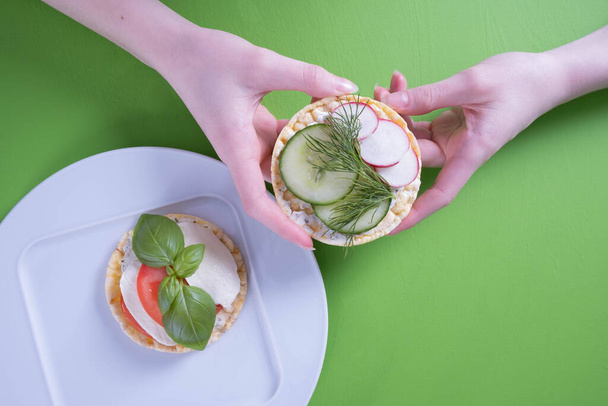 female hand holds a corn waffle and on it radish, cucumber on a green background - Foto, imagen