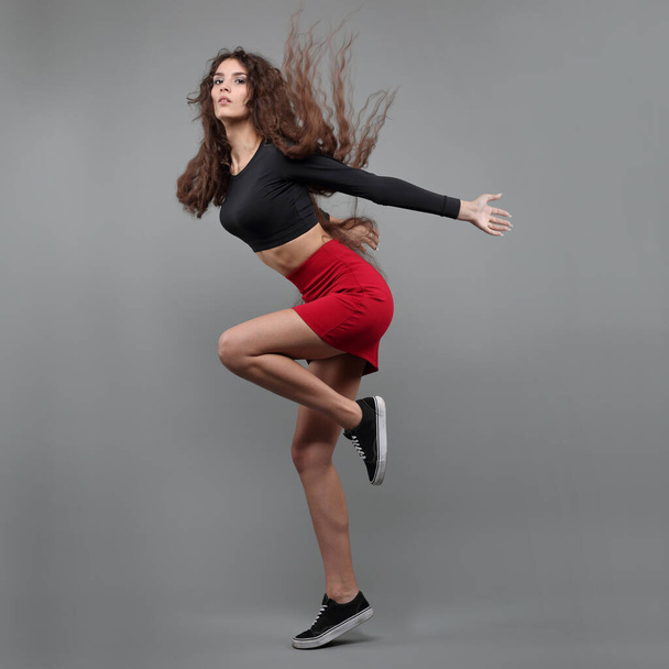 Beautiful girl dancer in a black top and red skirt on a gray background - Foto, immagini