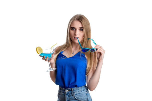 Dívka v jasně modrých džínách a blůze s modrým koktejlem s citrónem. Šťastná mladá dáma odpočívající s alkoholem. Izolováno na bílém pozadí - Fotografie, Obrázek