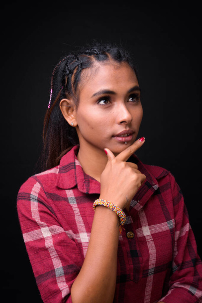 Studio shot of young beautiful Asian hipster woman with braided hair against black background - Zdjęcie, obraz