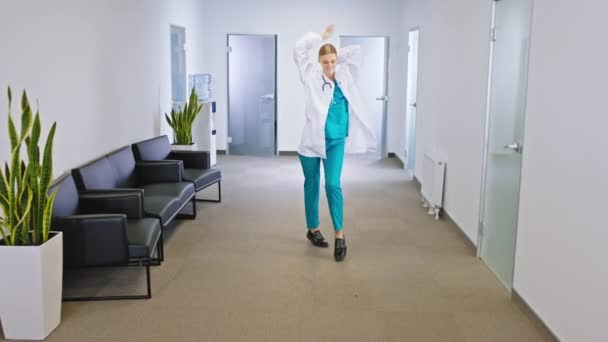 Moderno pasillo del hospital bonita mujer médico bailando carismático delante de la cámara ella está muy emocionada y sonriendo grande
 - Metraje, vídeo