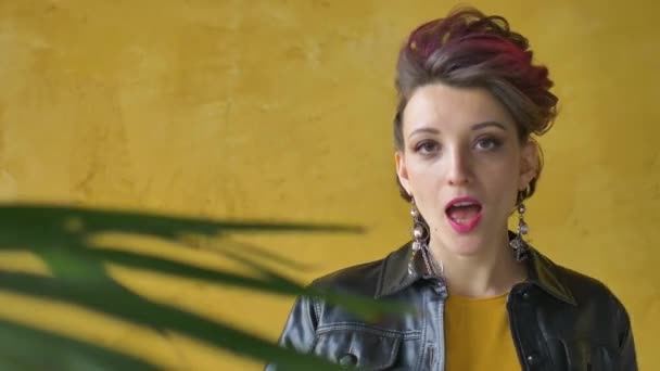 Lets rock concept. Portrait of excited beautiful woman with dark pink hair in casual yellow dress standing, looking at camera, showing rock and roll gesture. - Imágenes, Vídeo