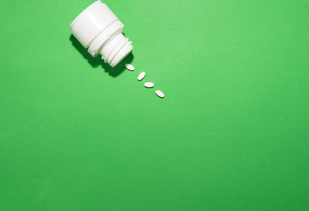 o frasco de medicamentos está em um fundo verde, algumas pílulas caíram e jazem
 - Foto, Imagem