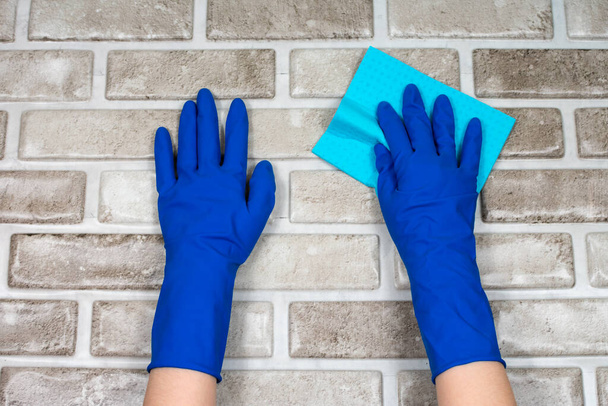 Рабочие руки в резиновых защитных перчатках с тряпкой, вытирая поверхность стола или стены в комнате, ванной комнате, кухне. Понятие чистоты
. - Фото, изображение