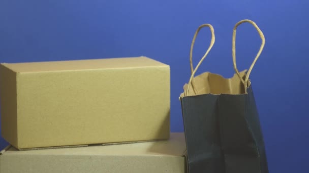 Money falling on packages. Online shopping concept. Carton boxes and paper bag on classic blue background. Stack of paper dollars. Black Friday. Sales on promo. Copy space - Footage, Video