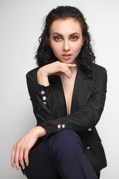 A beautiful young girl with wet curly hair in trousers and a black jacket on a bar chair. - Fotoğraf, Görsel