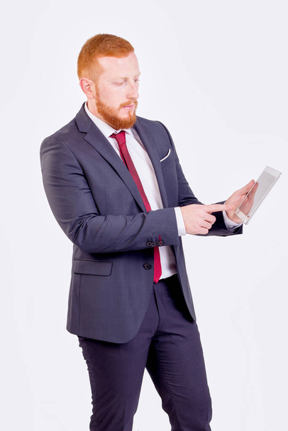 Un uomo d'affari dai capelli rossi che guarda un tablet. Indossa un completo rosso e cravatta.
 - Foto, immagini