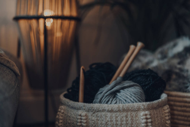 Close up of a basket full of yarn in the interior of a house, with large wooden knitting needles and crochet hook, shallow focus. - Photo, Image