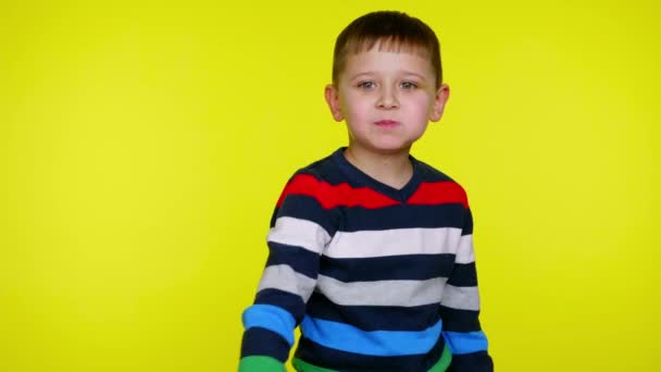 Child boy eats chocolate and throws a wrapper at the camera on yellow background - Footage, Video
