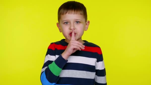 Schweigen. Kleiner Junge legt Zeigefinger an seine Lippen auf gelbem Hintergrund - Filmmaterial, Video