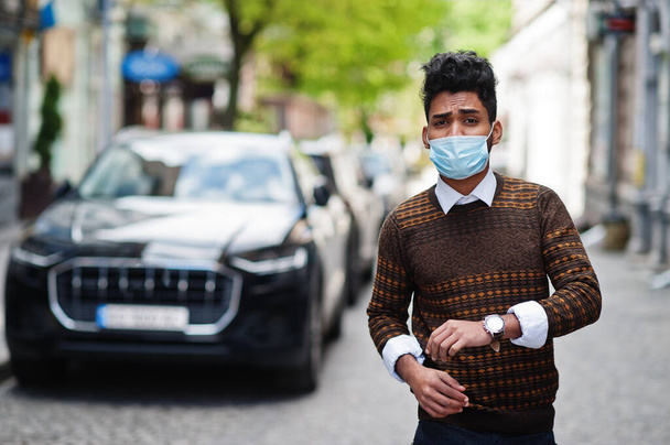 Coronavirus covid-19 concept. South asian indian man wearing mask for protect from corona virus posed against business car. - Photo, image