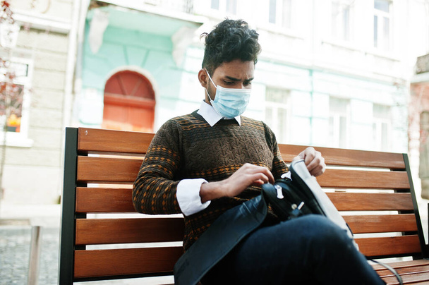 Coronavirus covid-19 concept. South asian indian man wearing mask for protect from corona virus sitting on bench. - Photo, image