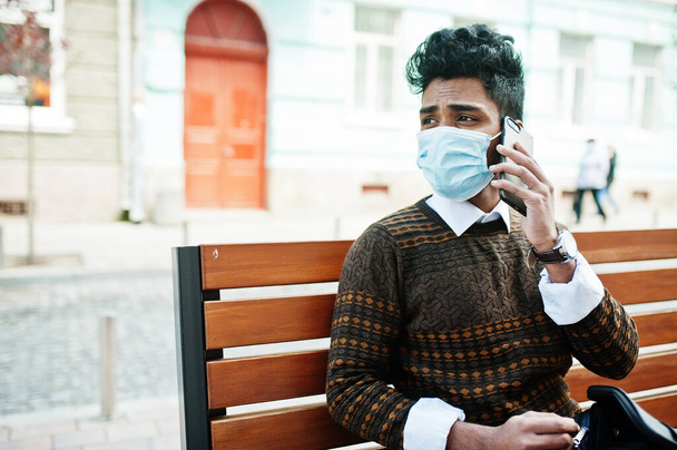 Coronavirus covid-19 concept. South asian indian man wearing mask for protect from corona virus sitting on bench with mobile phone. - Φωτογραφία, εικόνα