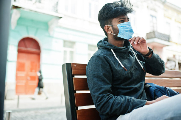 Coronavirus covid-19 concept. South asian indian man wearing mask for protect from corona virus sitting on bench. - Zdjęcie, obraz