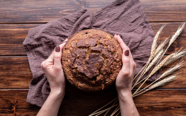Woman hands holding a loaf of homemade buckwheat bread top view on wooden background - Photo, Image