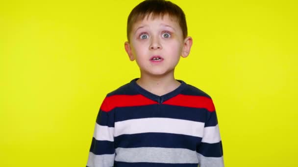 Mały chłopiec w kolorowym swetrze jest zaskoczony na żółtym tle - Materiał filmowy, wideo