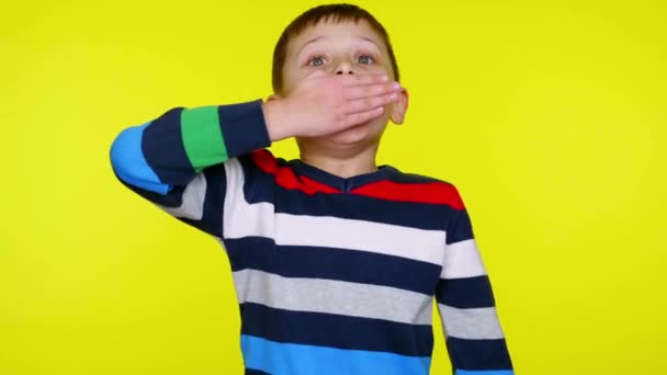kleine jongen is verbaasd sluiten van zijn mond met palm op een gele achtergrond - Video