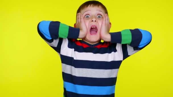 Μικρό αγόρι είναι έκπληκτος κλίνει παλάμες στα μάγουλα σε ένα κίτρινο φόντο - Πλάνα, βίντεο