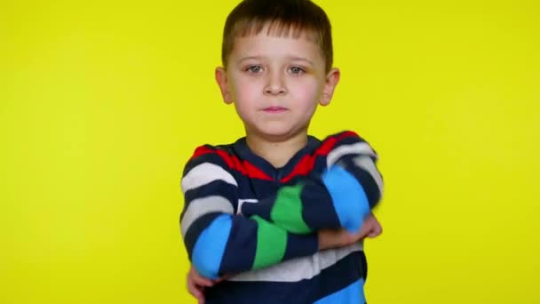Serieuze kleine jongen draait en vouwt armen over de borst op een gele achtergrond - Video