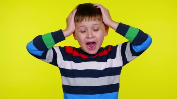 Little child boy screams holding his head in his hands on a yellow background - Footage, Video