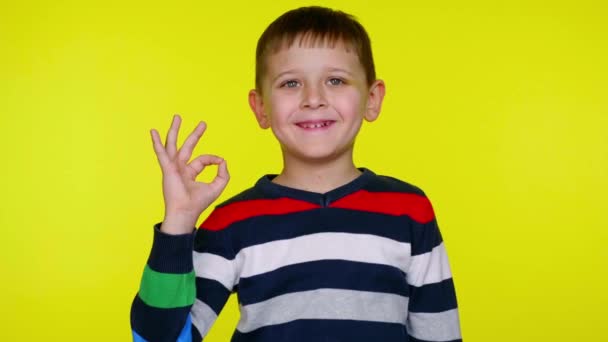 Alegre niño pequeño muestra okey y sonríe sobre un fondo amarillo
 - Metraje, vídeo
