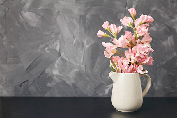 Pink flower in vase on black table on gray background. Close up - 写真・画像