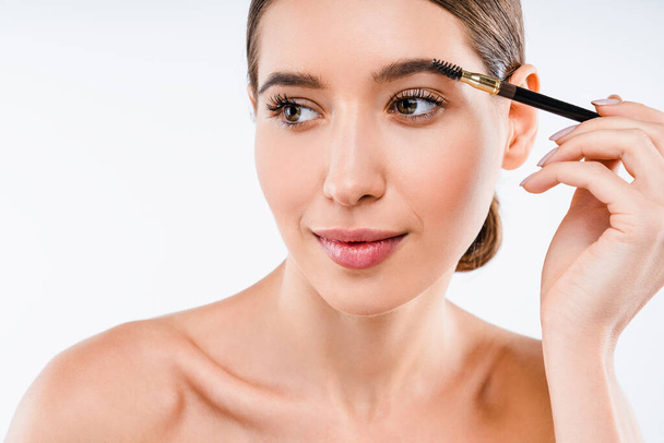 Young beautiful woman applying cosmetic brush on eyebrow, natural makeup on white background - Φωτογραφία, εικόνα