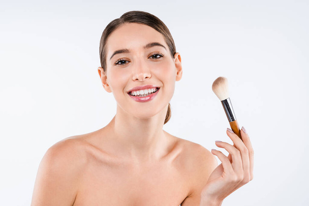 Beauty portrait of young smiling woman holding make up brush isolated over white background - Фото, изображение