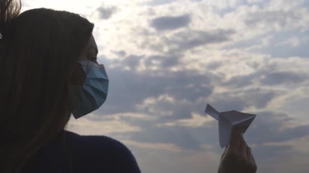 Το όμορφο κορίτσι με τη μάσκα πετάει χάρτινο αεροπλάνο σε εξωτερικό χώρο. αργή κίνηση - Πλάνα, βίντεο