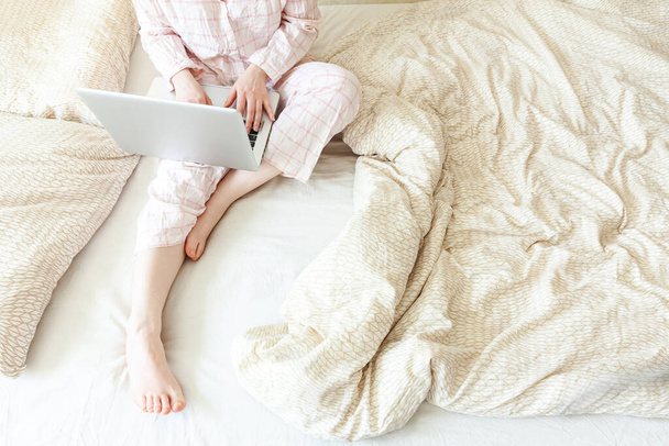 Mobiliroda otthon. Fiatal nő pizsamában otthon ül az ágyon és laptopon dolgozik. Lifestyle lány tanul idebent. Szabadúszó üzleti karantén koncepció - Fotó, kép