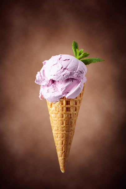 Черничное мороженое с мятой в вафельном конусе. Мороженое на коричневом фоне. - Фото, изображение