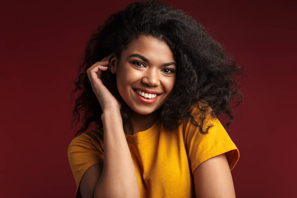 Image of beautiful brunette african american woman with curly hair smiling at camera isolated over red background - Photo, Image
