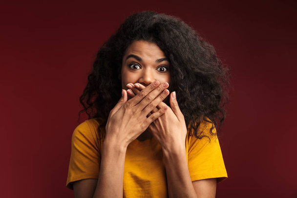 Image of emotional shocked young african woman posing isolated over dark red wall background covering mouth with hands. - Fotoğraf, Görsel