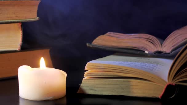 Κοντά στο ανοιχτό βιβλίο, ένα κερί καίει και χρωματιστές, μαγικές μύγες καπνού. - Πλάνα, βίντεο