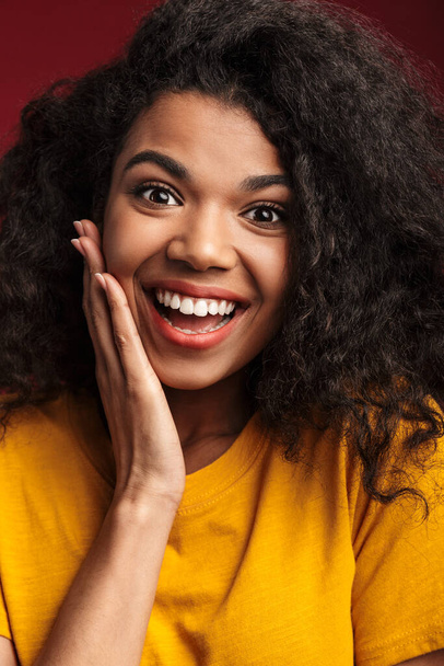 Зображення прекрасної брюнетки африканської американки з кучерявим волоссям посміхається в камері ізольований на червоному фоні - Фото, зображення