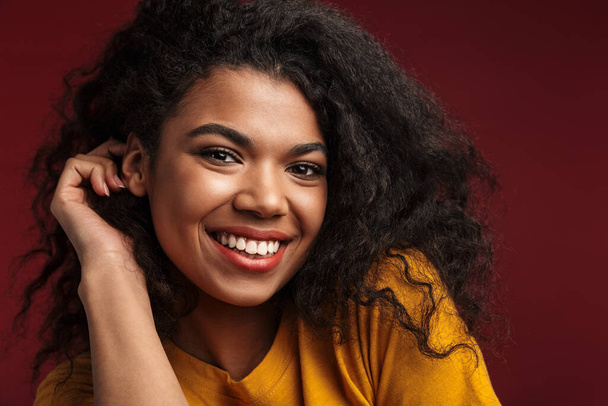 Image of beautiful brunette african american woman with curly hair smiling at camera isolated over red background - Foto, immagini