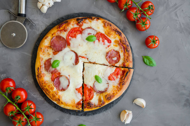 Hausgemachte italienische Pizza mit Tomatensauce, Salami, Käse und Basilikum auf einem Stein vor dunklem Hintergrund. Horizontale Ausrichtung. Ansicht von oben. - Foto, Bild