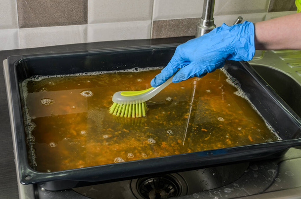 Housekeeper washes a baking dish with dishwashing liquid - Fotoğraf, Görsel